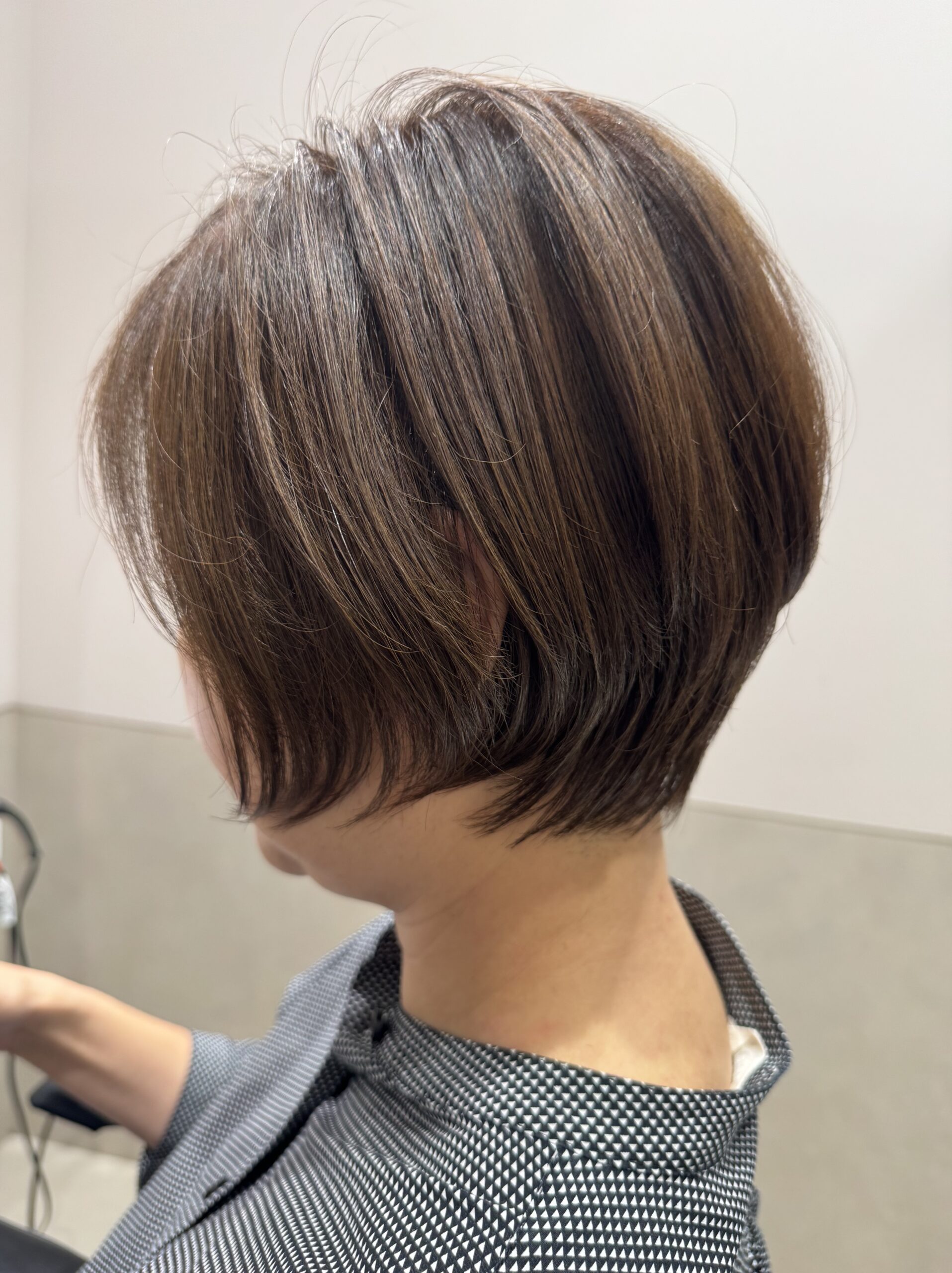 Rounded short bob haircut with natural brown hair color, side-back view showing a compact neckline