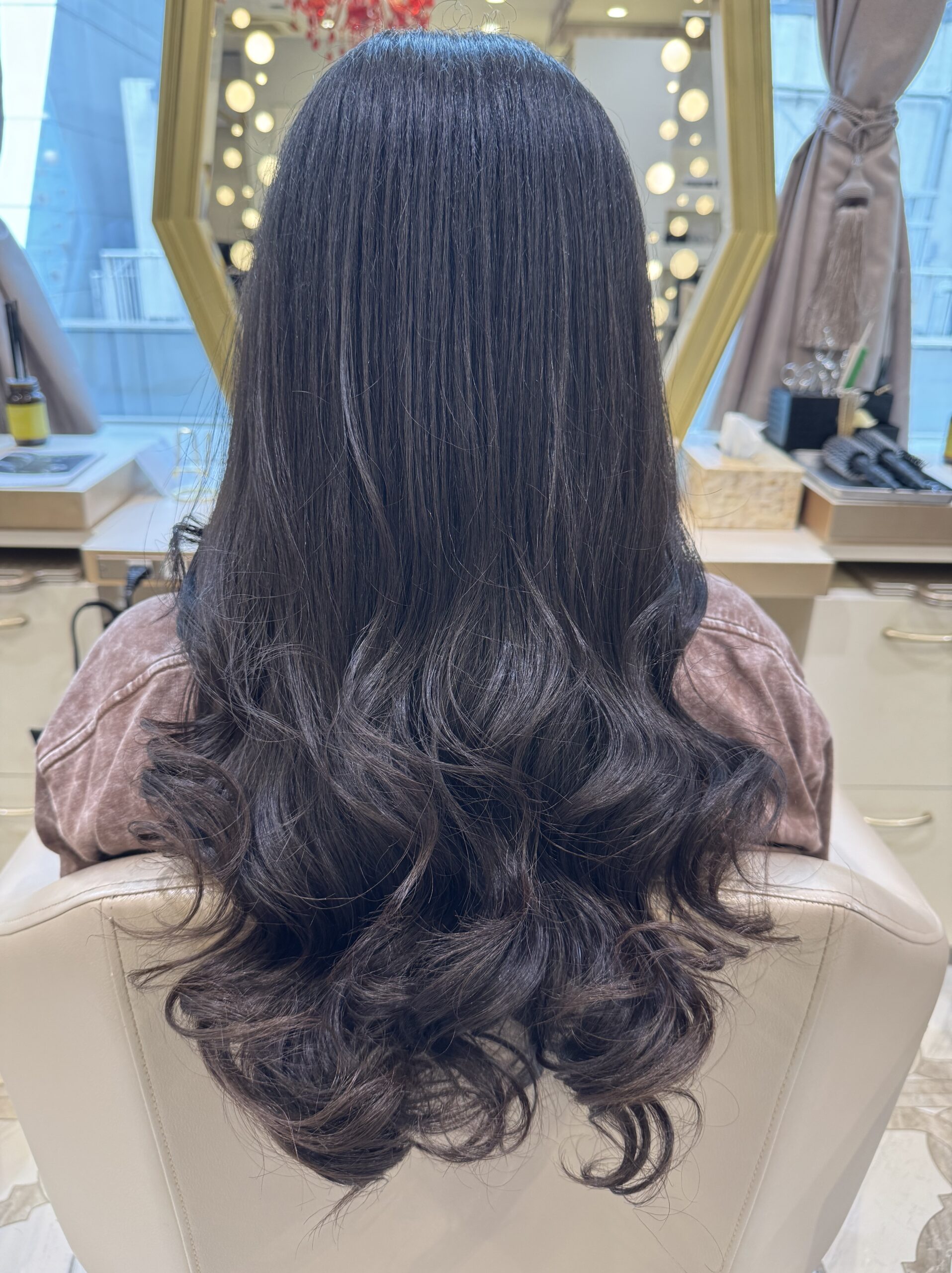 Long dark hair with glossy, smooth lengths and soft defined curls at the ends — straight back view after treatment