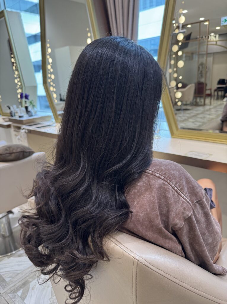 Side view of long dark hair with smooth texture and soft curls after treatment and styling