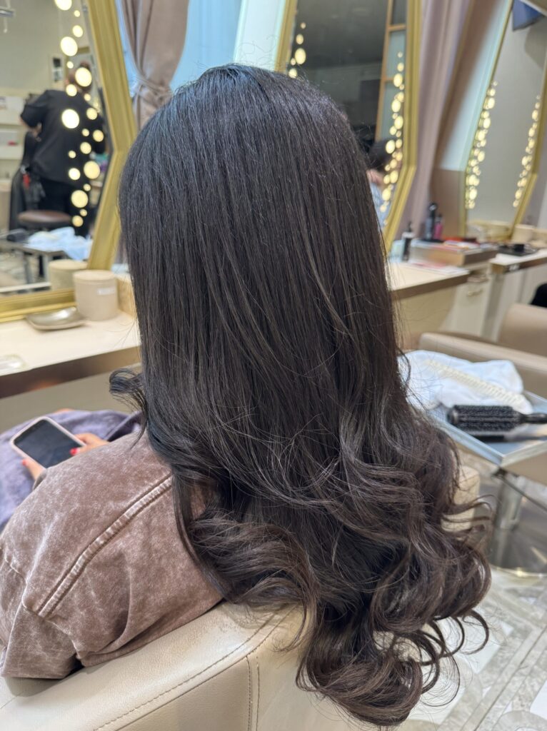 Side-back view of long dark hair with shine through the mid-lengths and soft curled ends